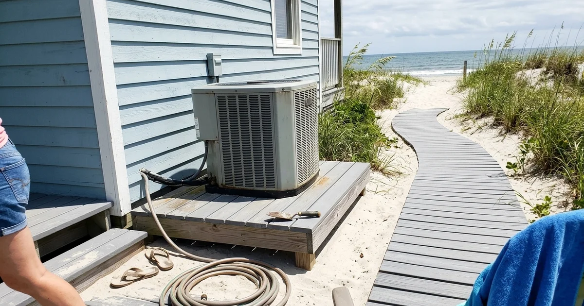 Outdoor AC on a raised stand behind a beach house with dunes behind