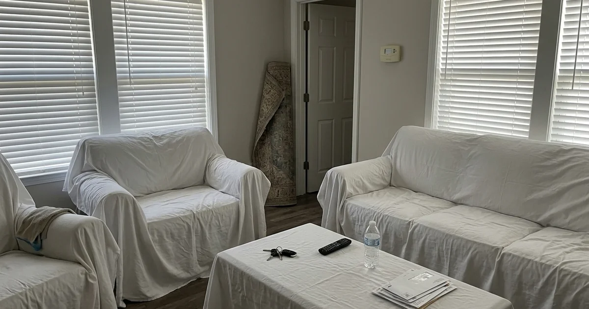 Closed-up beach house living room with sheets over furniture and blinds down