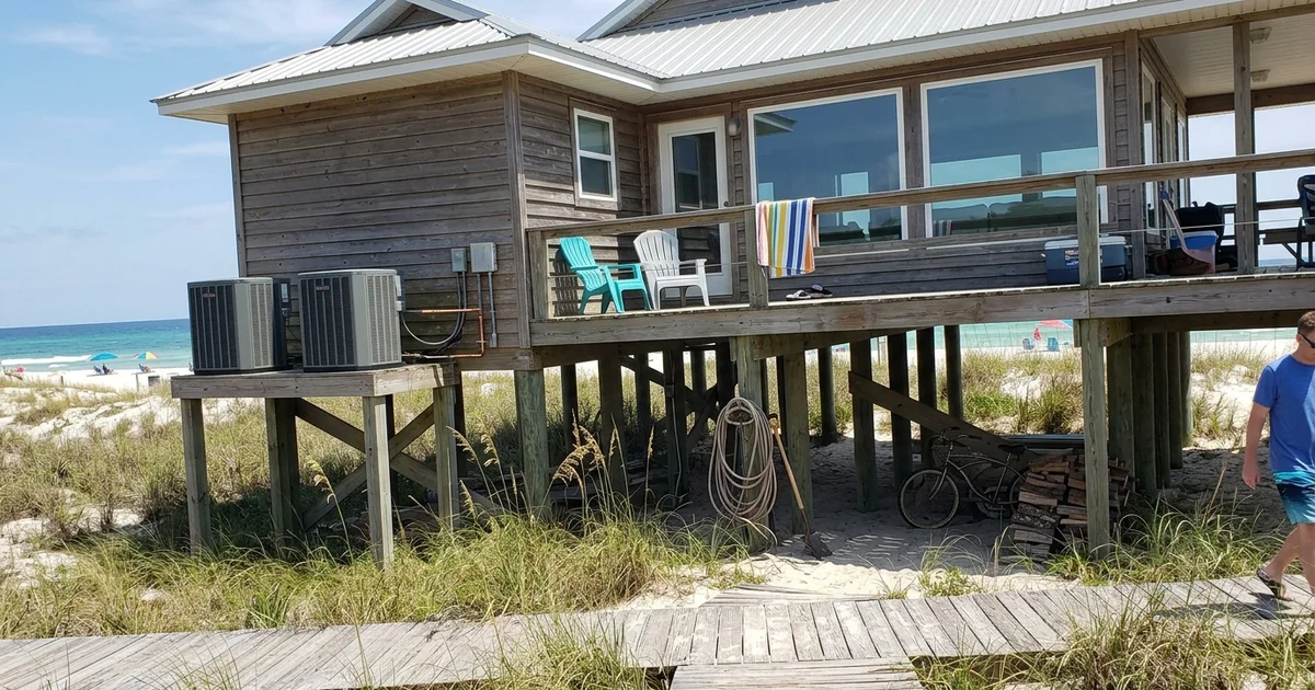 Raised beach house on pilings with large Gulf-facing windows at midday