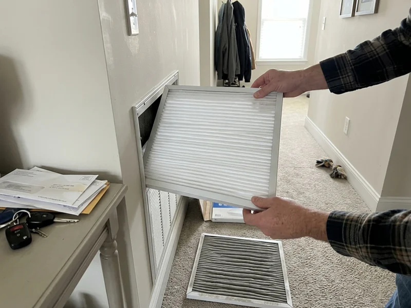 New pleated filter being installed in a return grille with the old dirty filter nearby