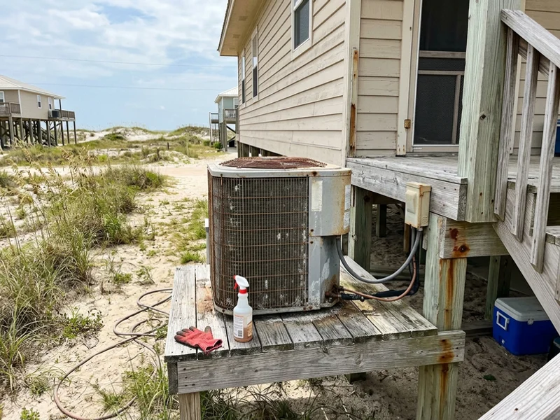 Salt-weathered AC condenser on a raised platform beside a coastal Alabama home