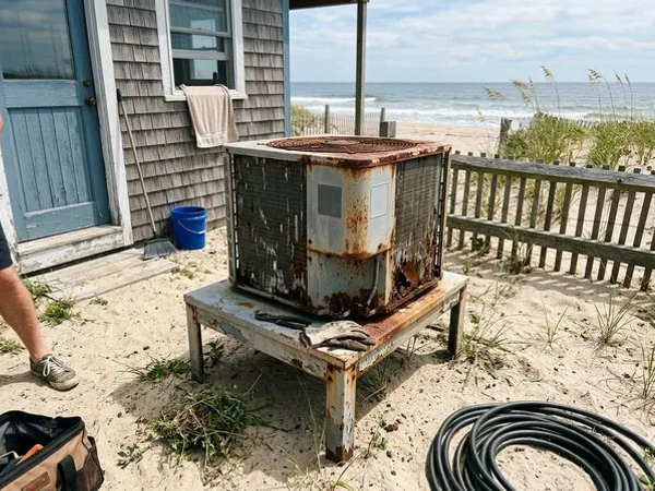 Old rusted AC condenser with corroded fins beside a beach cottage