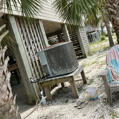 Salt-weathered AC condenser on a wooden stand beside a raised Gulf Shores beach house